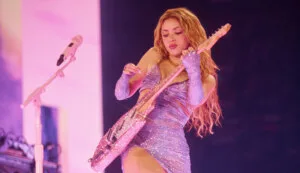 Artista tocando una guitarra eléctrica brillante durante un concierto en vivo con iluminación rosa y vestuario brillante.